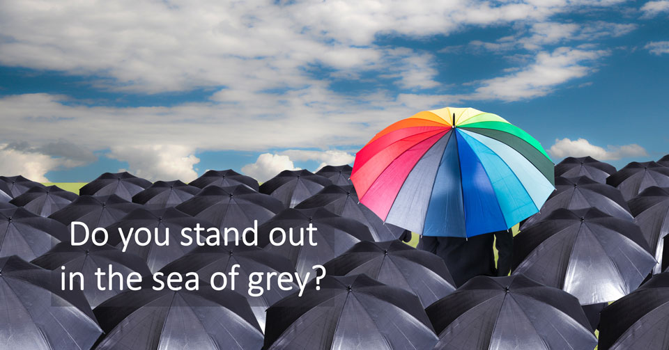 One rainbow umbrella standing out among a sea of black ones